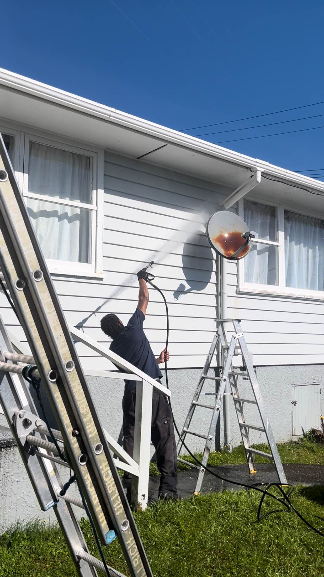 A TrueShine technician soft washing the weatherboard cladding of a Wellington home from a ladder